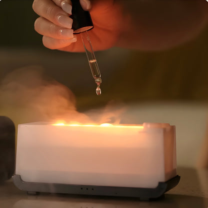 Hand using a dropper to add liquid to a white rectangular LED-flame aromatherapy diffuser and humidifier